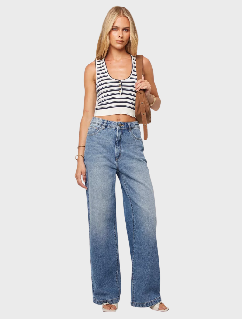 A woman in wide-legged jeans and a striped top stands confidently, showcasing a casual yet stylish outfit.