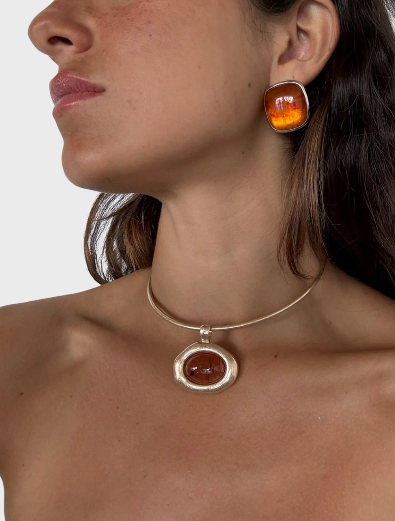 A gold necklace adorned with a large, vibrant orange stone, showcasing a blend of elegance and bold color.