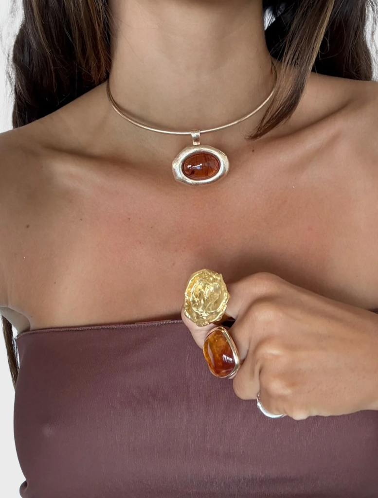 A gold necklace featuring a striking orange stone, designed to enhance any outfit with its bold elegance.