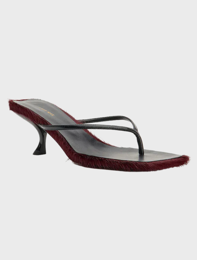 A burgundy pony stands in a grassy field, showcasing its shiny coat and alert expression.