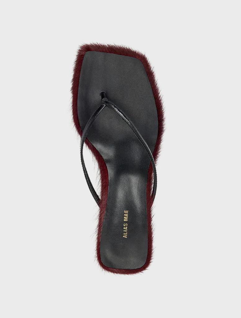 A pair of black sandals adorned with red fur, labeled as Arli - Burgundy Pony.