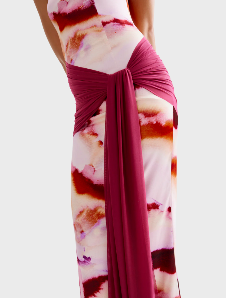 A woman dressed in a pink mineral print gown stands in front of architectural pillars, embodying grace and poise