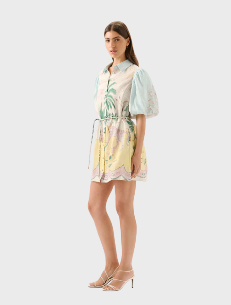 The Berkley Mini Dress - Utopia is worn by a model, showcasing a colorful pattern of palm trees and flowers.