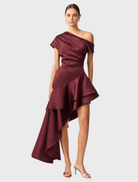 Livia Gown in berry satin features an asymmetric hem, offering a stylish and modern silhouette.