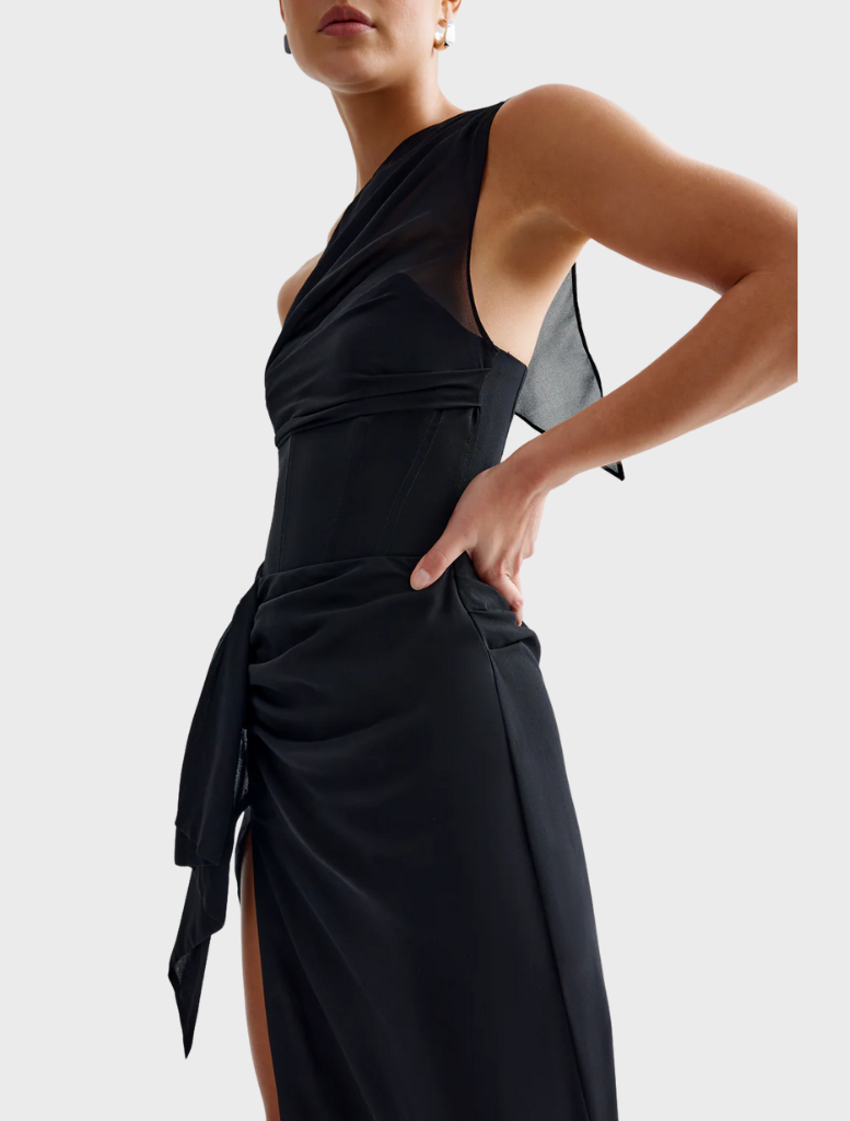 A woman in a sleek black dress stands next to a vintage car, embodying sophistication and classic charm.