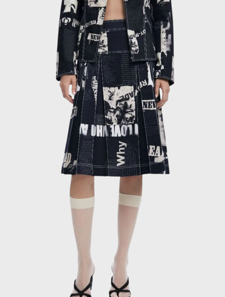 A model displays a black and white print jacket paired with a black Newspaper Pleated Midi Skirt.