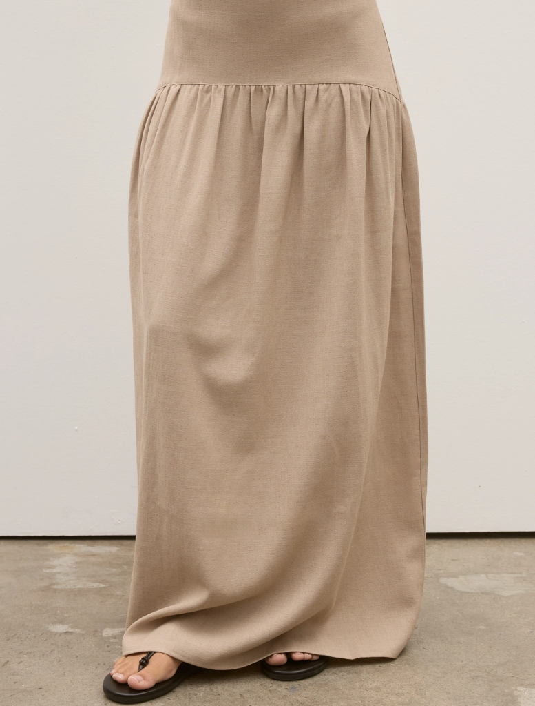 Back view of a woman in a tan dress, showcasing the Delphine Skirt in Nude.
