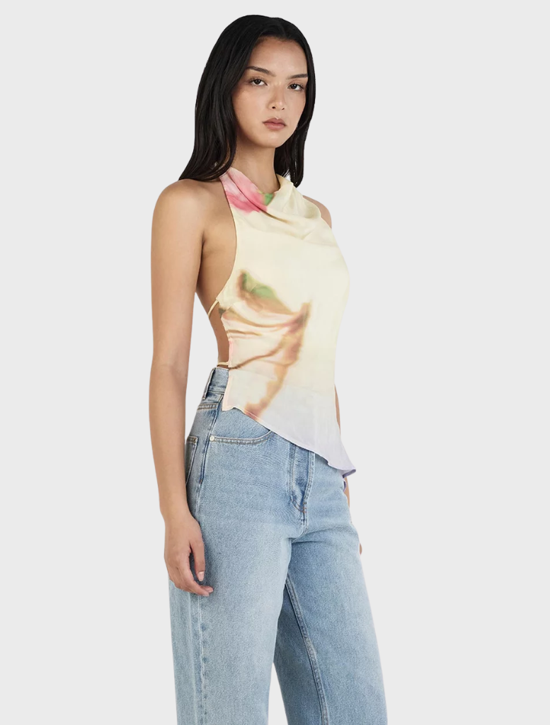 The Iris Halter Top in Golden Drift is worn by a model, featuring a sunny yellow hue adorned with a floral design.