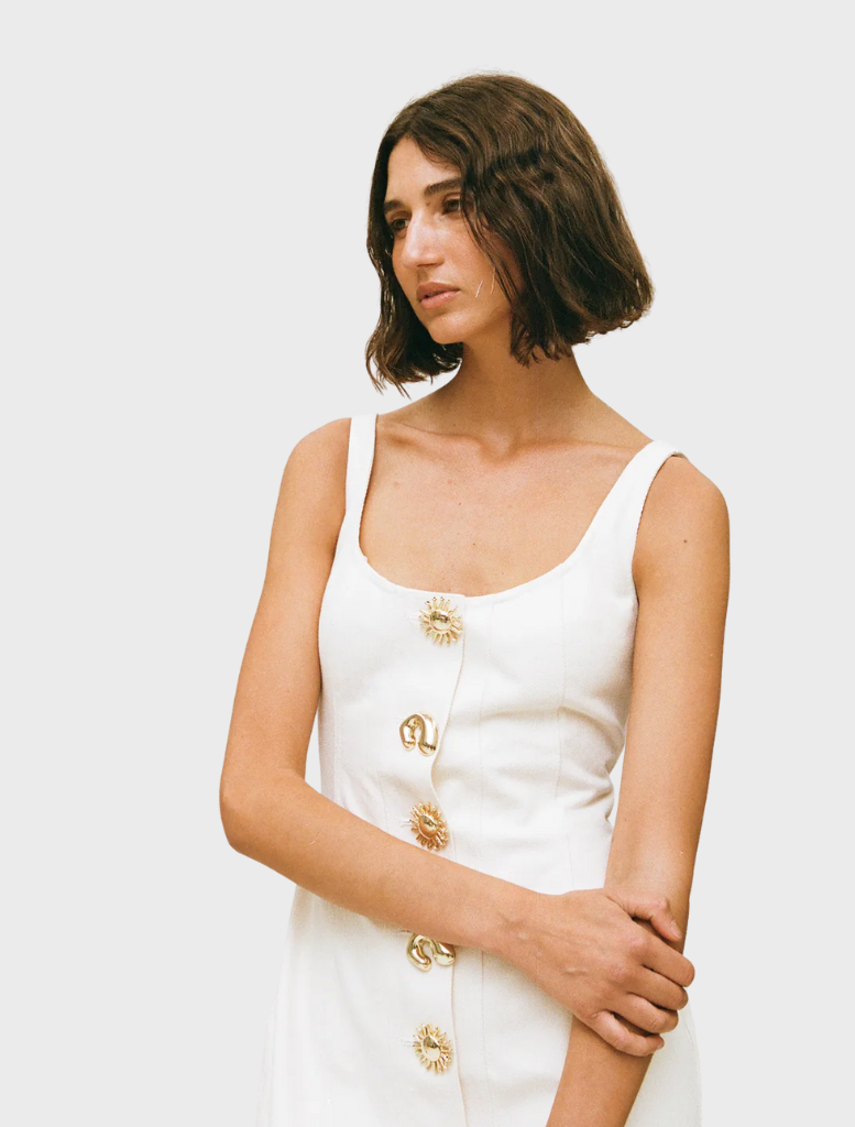 A woman in a white Sibel Denim dress and sandals poses gracefully, highlighting her chic summer fashion choice.