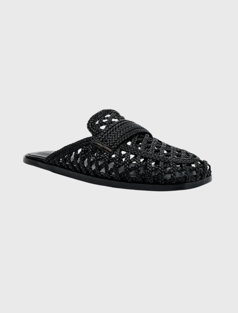 Krissy, a black woven mule, showcases a square toe, wide crossover strap, and an open back for effortless slip-on style.