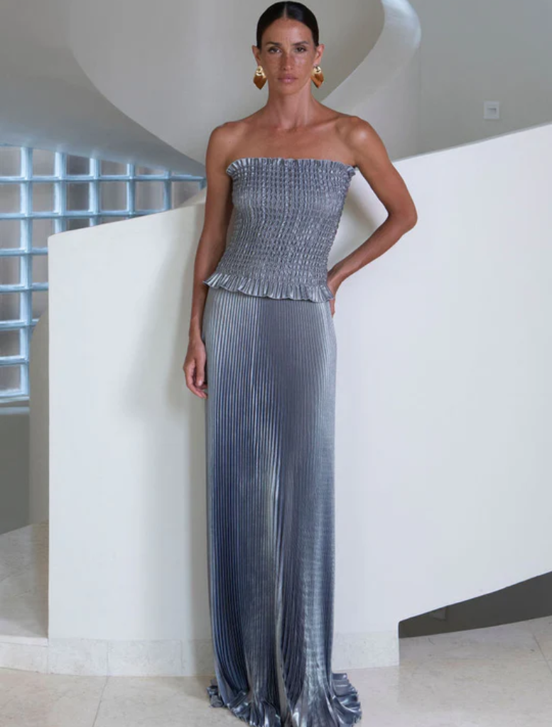 A woman wearing a shimmering metallic dress stands gracefully on a stairway, highlighting her fashion choice.