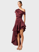 The Livia Gown in burgundy satin showcases an asymmetric hem, perfect for formal occasions.