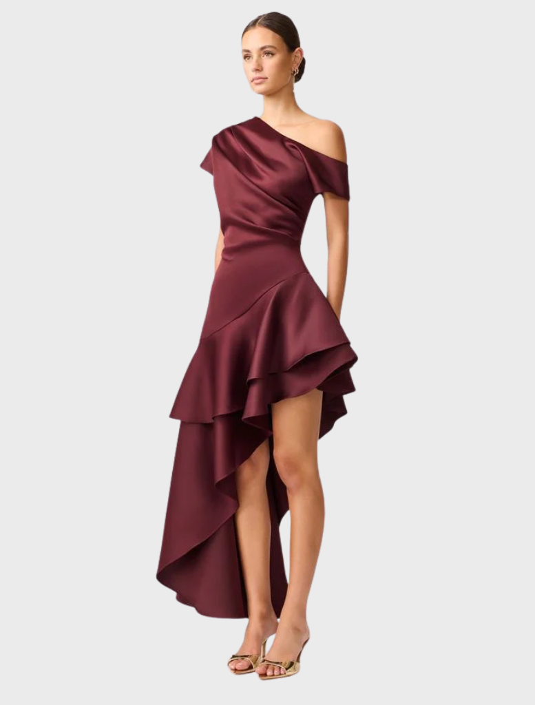 The Livia Gown in burgundy satin showcases an asymmetric hem, perfect for formal occasions.