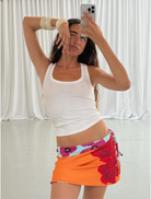 A woman in a white tank top paired with an orange skirt poses, highlighting her stylish summer attire.