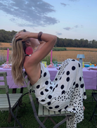 A woman in a polka dot dress stands before a mirror, preparing for an event while admiring her reflection.