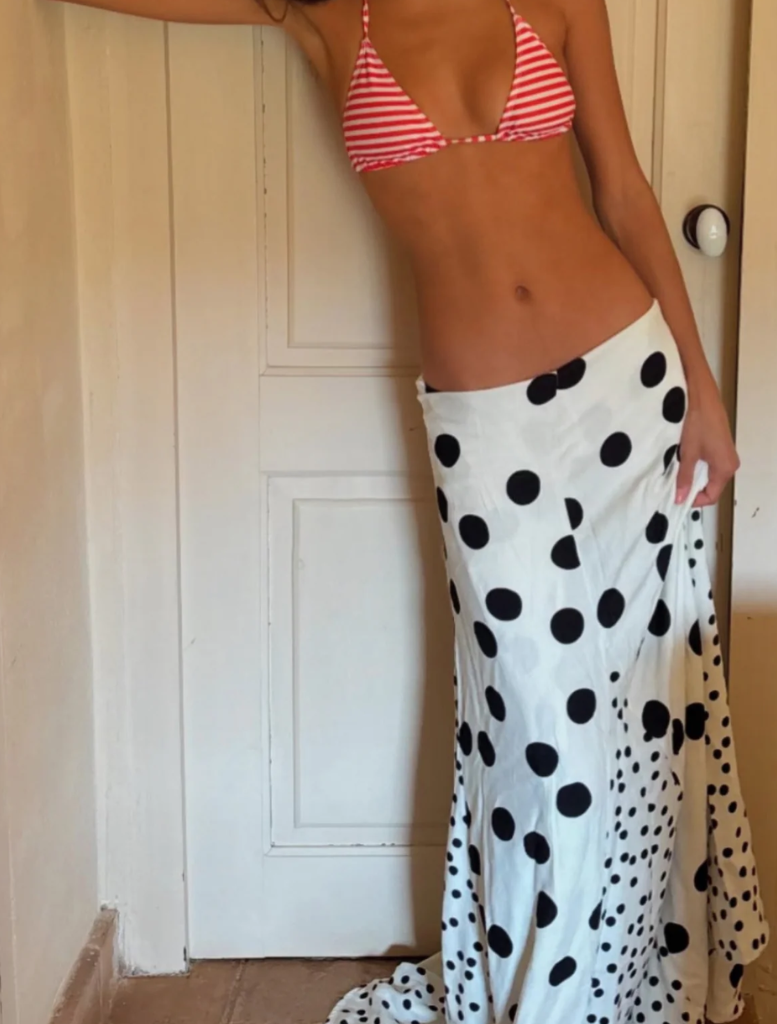 A woman wearing a polka dot dress poses in front of a mirror, looking at her reflection with a smile.