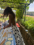 A woman dressed in polka dots stands in front of a mirror, gazing at her reflection with a thoughtful expression.