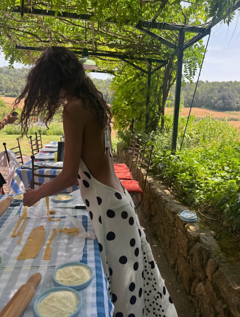 A woman dressed in polka dots stands in front of a mirror, gazing at her reflection with a thoughtful expression.