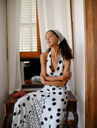 A woman in a polka dot dress stands before a mirror, checking her appearance and smiling at her reflection.
