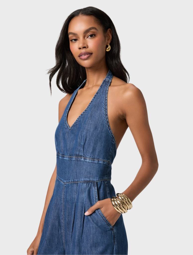 A stylish jumpsuit with a flattering silhouette, featuring a halter neck and wide legs in a soft, dark wash denim fabric.