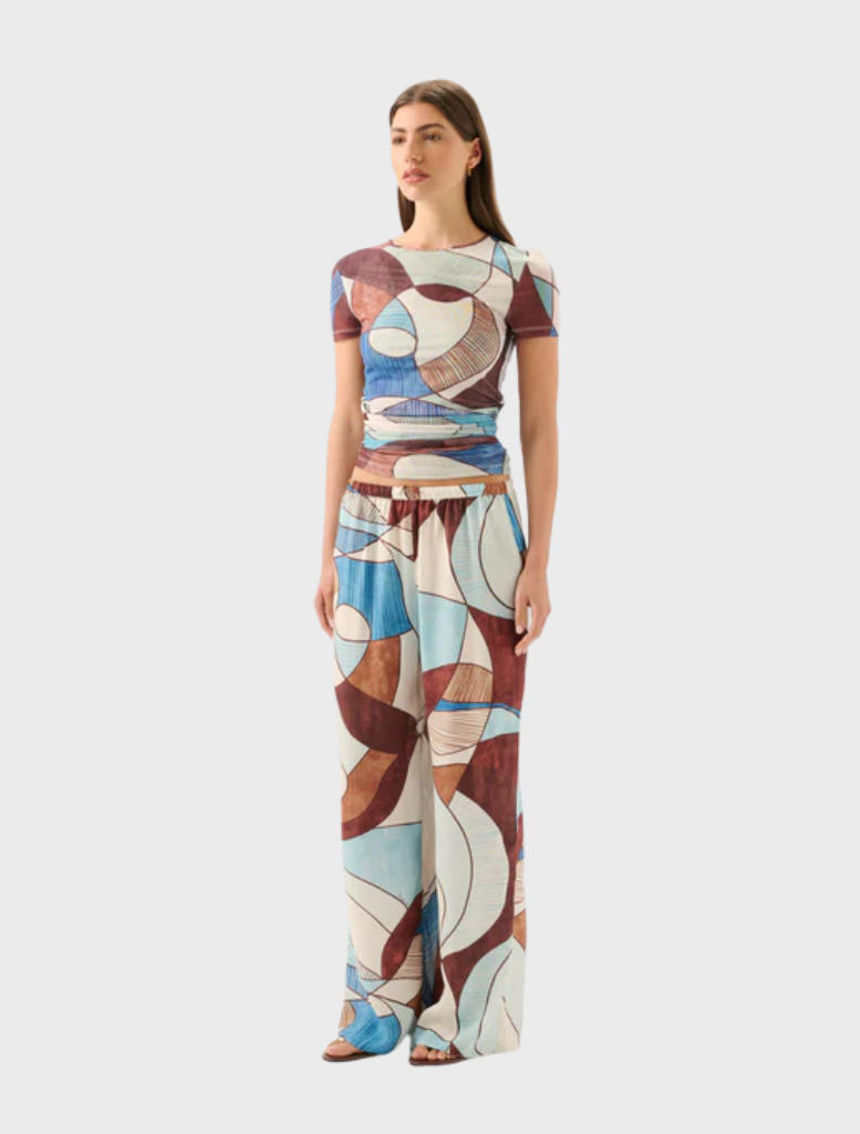 A woman showcases the Marley Mesh Tee - Playa, adorned with colorful abstract patterns on a stylish t-shirt.