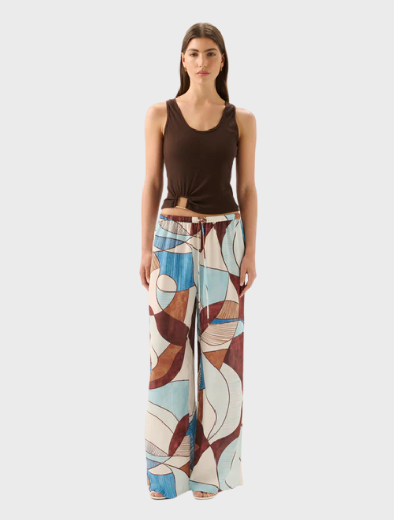 A woman in a brown tank top and blue and white patterned pants, showcasing the Miles Pant - Playa style.