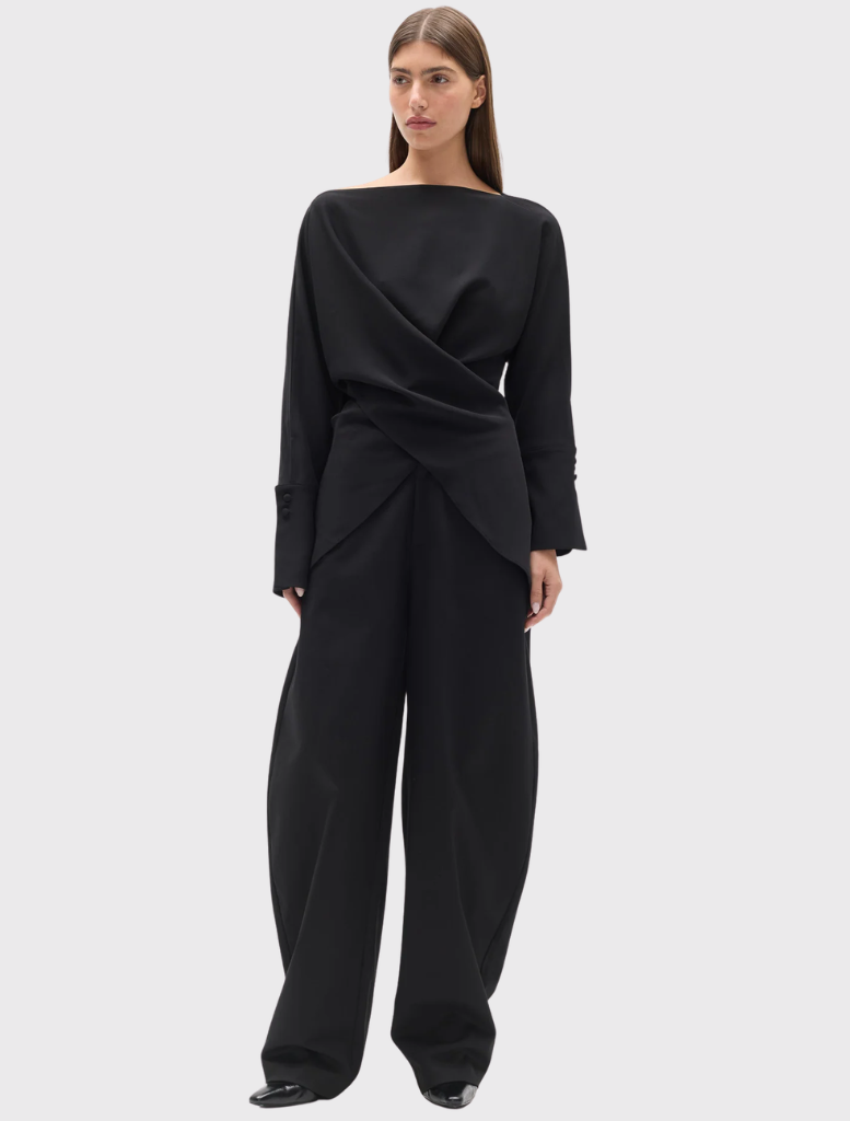 Black Novalyn Top with boat neckline, draped crossover front, self-tie waist, long sleeves, and wide buttoned cuffs.