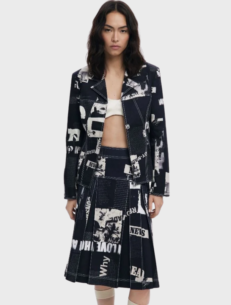 The model is dressed in a black and white print skirt and jacket, highlighting the Newspaper Pleated Midi Skirt in black.