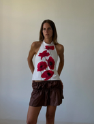 A woman stands in front of a white wall, wearing a fashionable poppytop