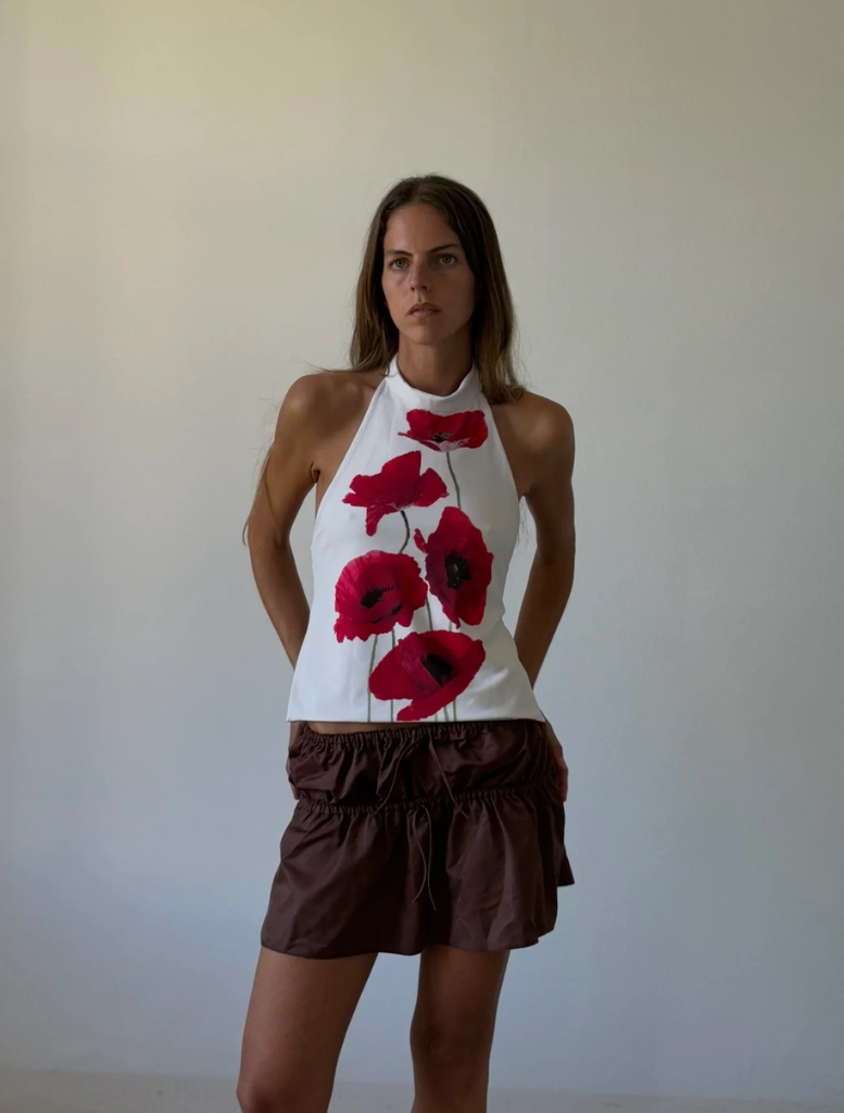 A woman stands in front of a white wall, wearing a fashionable poppytop
