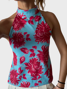 A woman wearing a blue and pink floral top, smiling and standing against a neutral background.