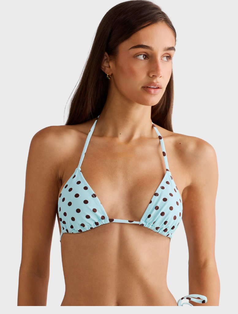 A blue polka dot Rio top hanging, featuring a playful pattern and modern cut, perfect for casual wear.