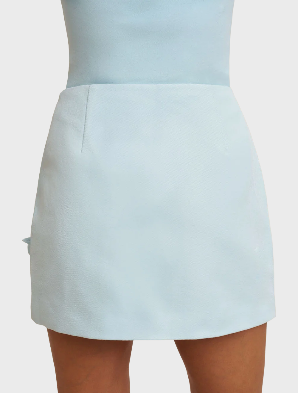 A-line mini skirt in ice blue, showcasing handmade rosettes on the front, constructed from structured twill and fully lined.