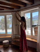 A woman in a red and black dress stands confidently on a stone wall, showcasing her stylish outfit against a natural backdrop.