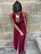 A woman in a red and black dress stands confidently on a stone wall, showcasing her stylish outfit against a natural backdrop.