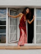 A woman dressed in red and black stands on a stone wall, creating a bold visual contrast with her surroundings.