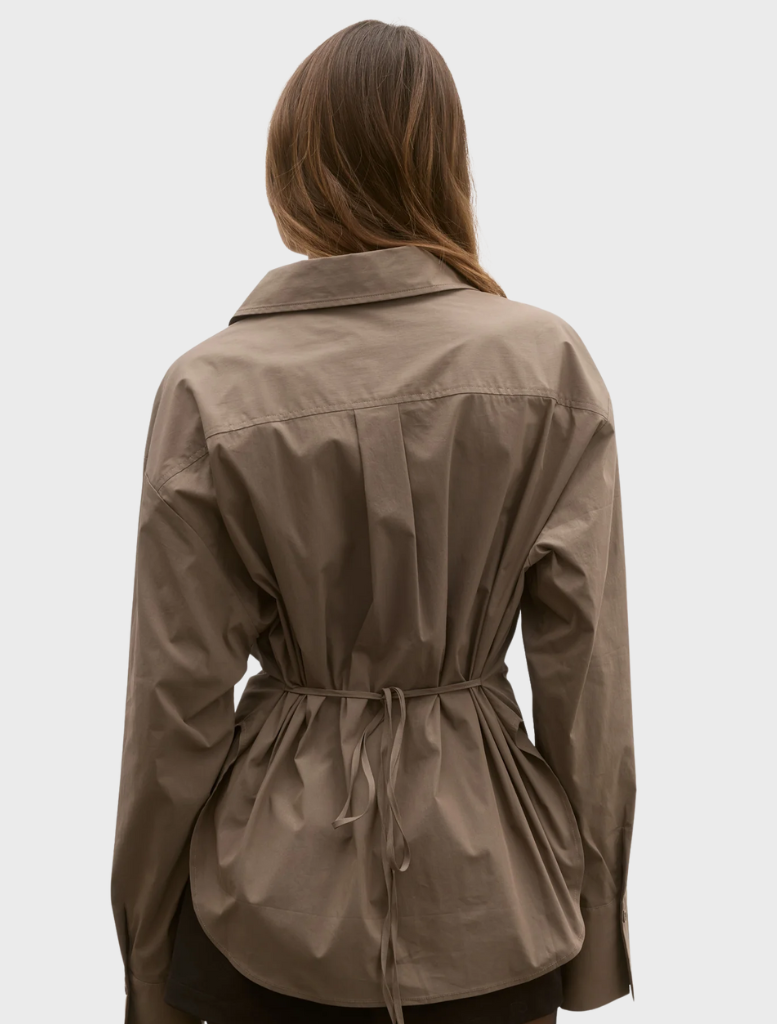 A model wears a brown shirt and shorts, presenting a casual look against a simple, unobtrusive background.