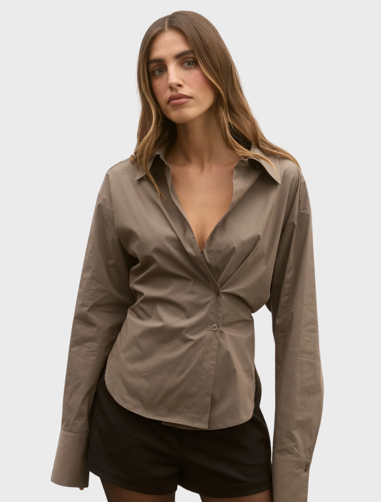 A model is dressed in a brown shirt and matching shorts, posing confidently against a neutral background.