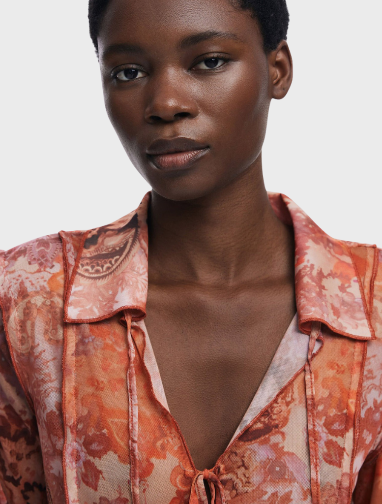 Model displays a multi-colored long-sleeve blouse with an orange and brown paisley print, highlighting its unique design.