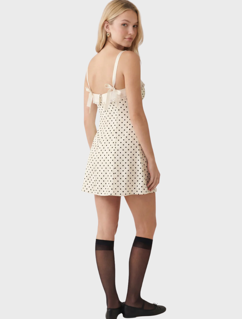 Elegant white mini dress adorned with black polka dots, designed with a fitted bodice and flared skirt for a stylish look.