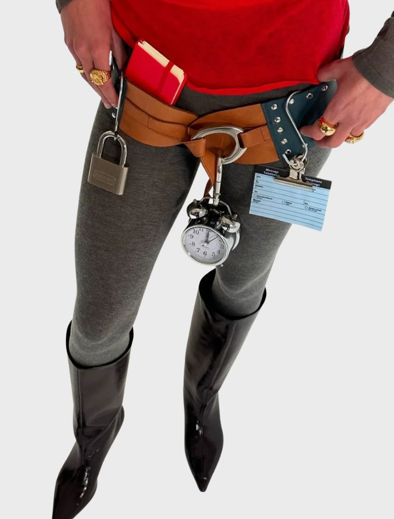 A woman in boots holds a multicolour Nuvola belt, showcasing a watch and other accessories.