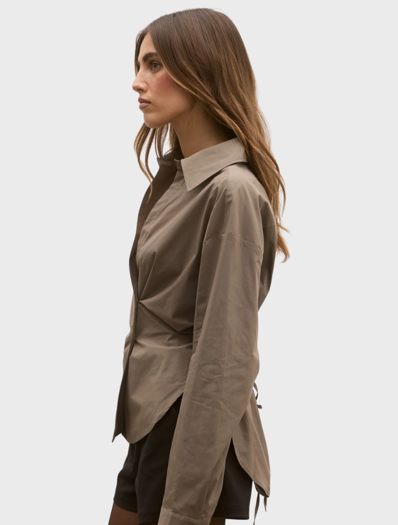 A model is dressed in a brown shirt and matching shorts, showcasing a casual summer outfit.