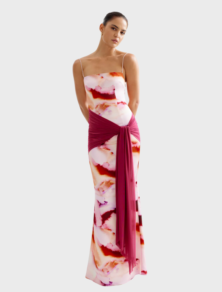  A woman in a flowing pink mineral print dress stands before grand pillars, highlighting her elegant silhouette.