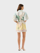 The Berkley Mini Dress - Utopia is modeled, featuring a bright pattern of palm trees and flowers.