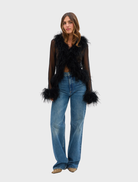 A model showcases the black Gigi Feather Blouse, featuring decorative feathers for a chic and fashionable look.