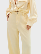  A woman wearing pale yellow pants and a matching blouse, showcasing a stylish outfit.