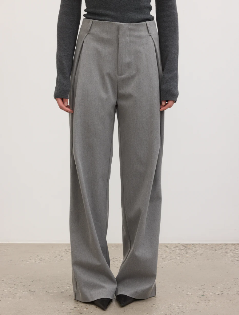 The model displays a chic outfit featuring grey trousers and a black top, ideal for various occasions.