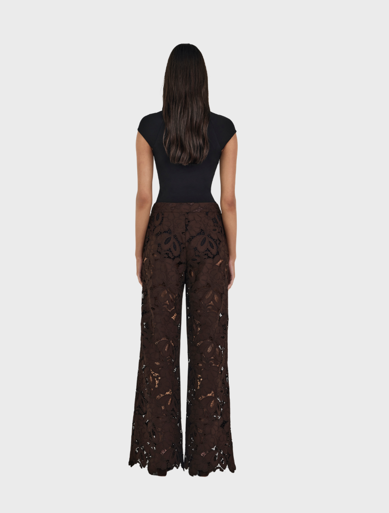 A woman dressed in a black top paired with brown Lotus Lace pants, showcasing a stylish outfit.