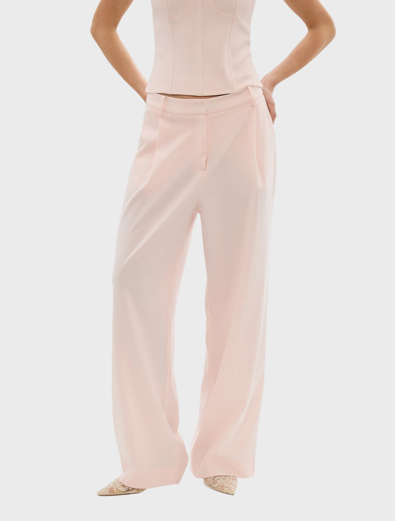 A woman wearing a pale pink top and pants, showcasing the Cleo Pant style.
