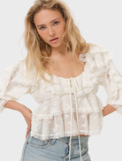 Lilou top in cream color, elegantly draped on a hanger, highlighting its chic design and soft material.